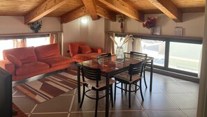 Een knus vertrek met een houten plafond, een rode bank, een eettafel met stoelen en een uitzicht door grote ramen.