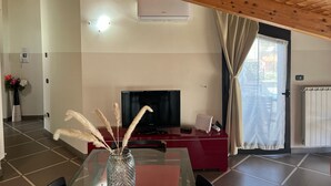 Een kamer met een houten plafond, een flatscreentelevisie, een rode bank, een glazen salontafel en een vaas met gedroogde planten.