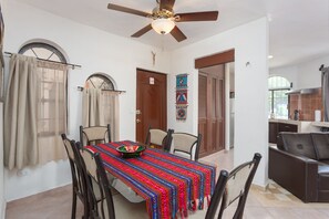 A dining area with a table set for four, a ceiling fan, and a view into the kitchen.