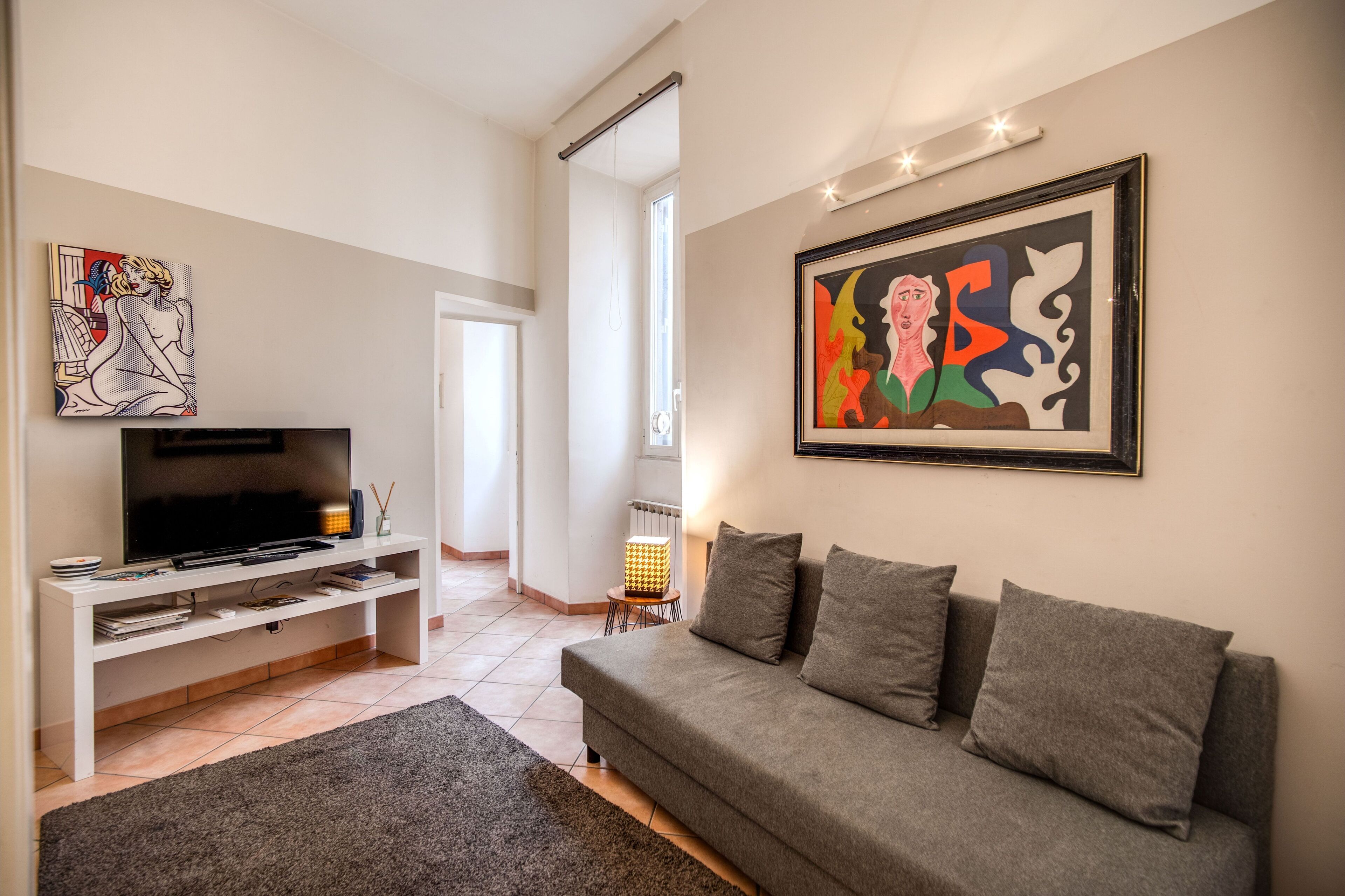 A modern living room with a grey sofa, a flat-screen TV on a white stand, and two abstract paintings on the walls.