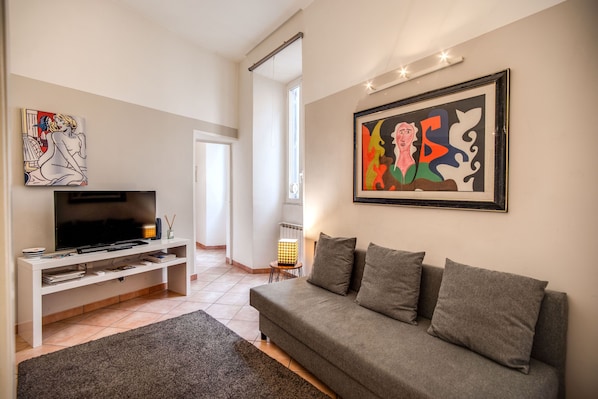 A modern living room with a grey sofa, a flat-screen TV on a white stand, and two abstract paintings on the walls.