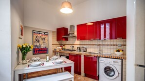 A compact kitchen with red cabinets, a washing machine, and a dining area with a table set for two. - Campo dei Fiori, Lovely Apartment "easy Life In Rome" (Rome)