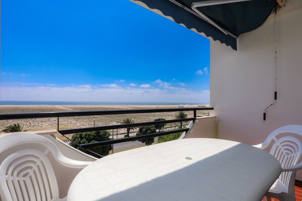 A balcony with a table and chairs, overlooking a coastal landscape.