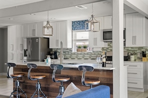 A modern kitchen with white cabinets, a stainless steel refrigerator, a built-in oven, and a bar area with stools.