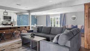 En moderne stue med en grå hjørnesofa, et sofabord og en bar med barstole.