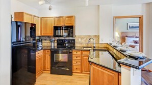 A modern kitchen with wooden cabinets, a black refrigerator, a microwave, an oven, and a sink.