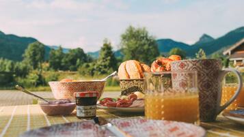 A breakfast table with bread, eggs, and a jug of orange juice, set against a mountainous backdrop.