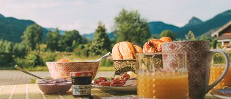 A breakfast table with bread, eggs, and a jug of orange juice, set against a mountainous backdrop.