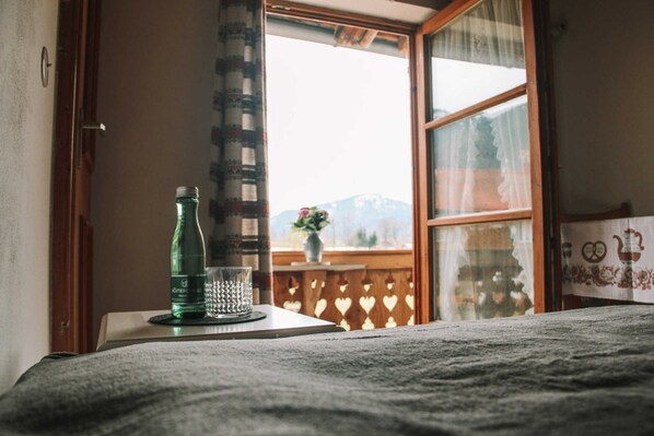Ein Zimmer mit einem Bett, einem Fenster mit Bergblick, einer Flasche und einem Glas auf einem Tisch.