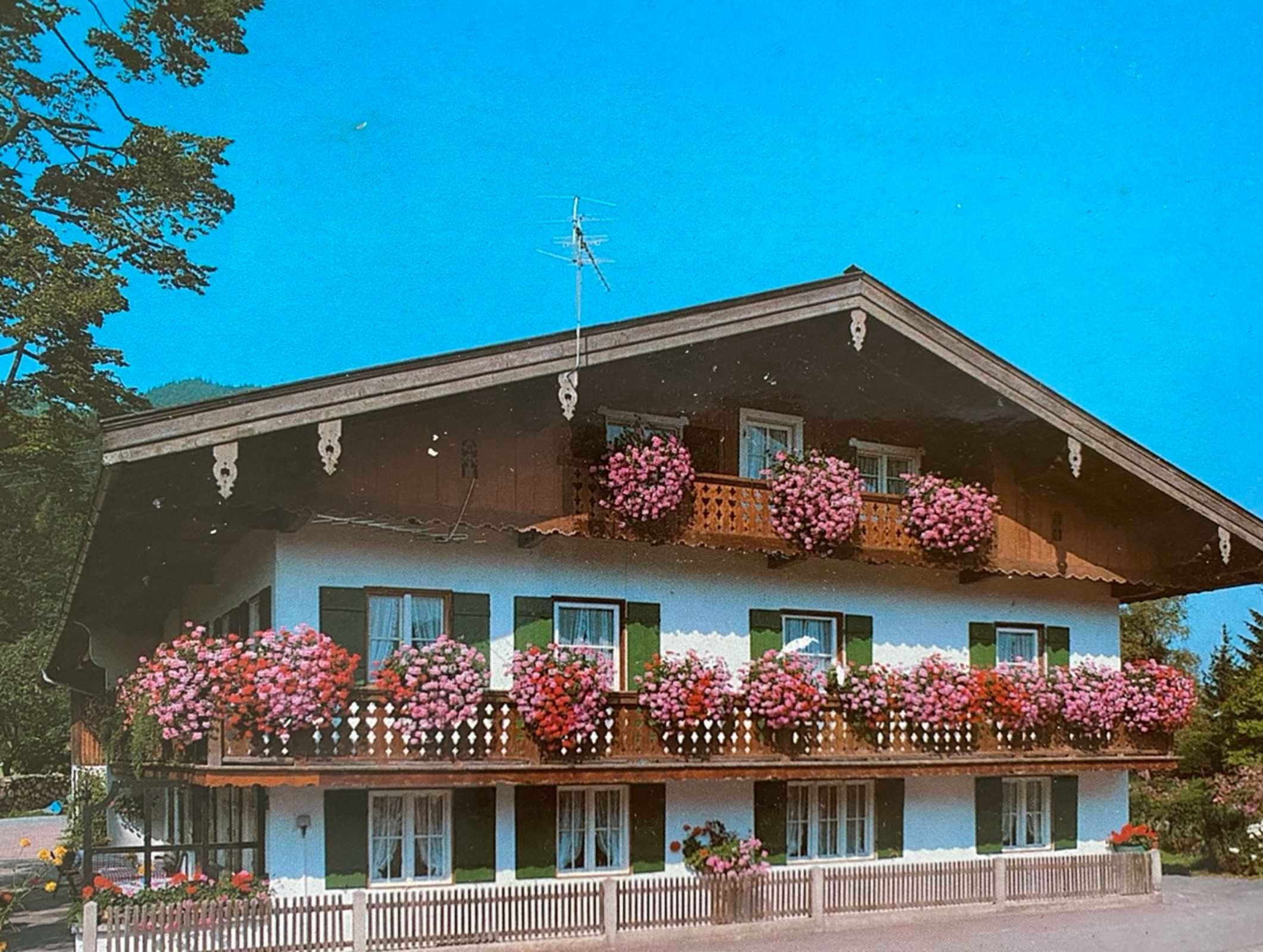 A two-story building with balconies adorned with flowers, a sloped roof, and a visible antenna.