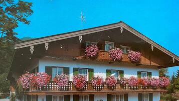 A two-story building with balconies adorned with flowers, a sloped roof, and a visible antenna.