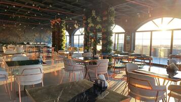 A spacious indoor area with multiple seating arrangements, including tables and chairs, and large windows offering views of the outside.