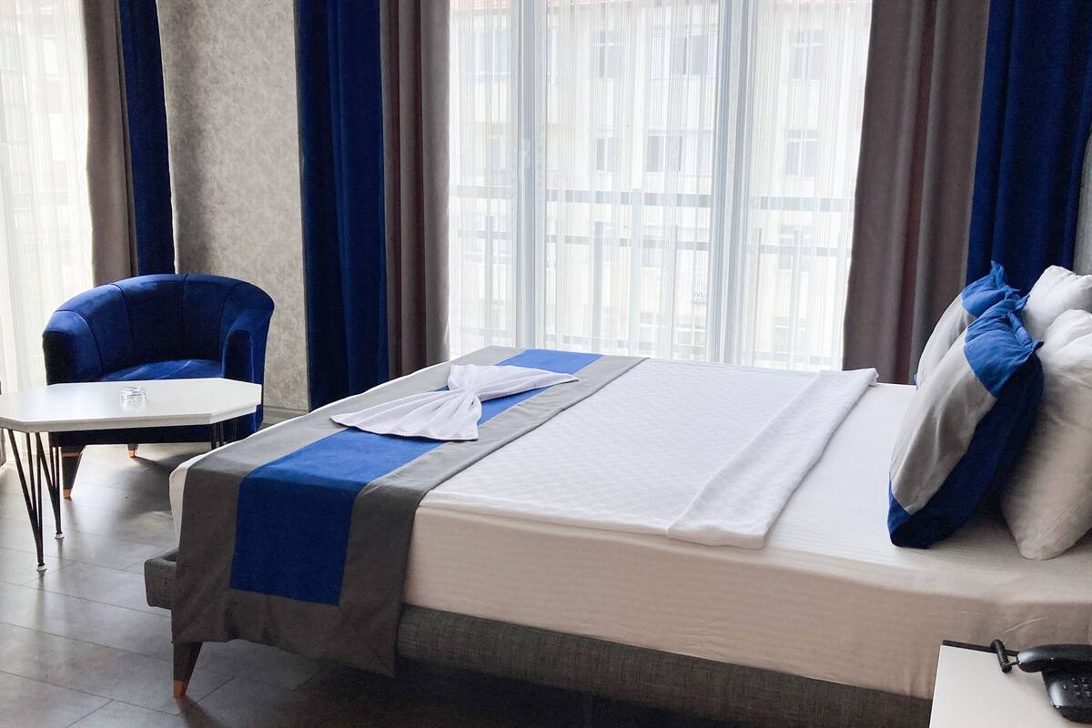 A hotel room with a bed, a chair, a table, and a phone.
