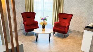 Una habitación con dos sillas rojas, una mesita blanca y un jarrón con flores.
