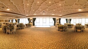 Un amplio salón de banquetes con mesas y sillas redondas, una alfombra estampada y un techo decorativo.