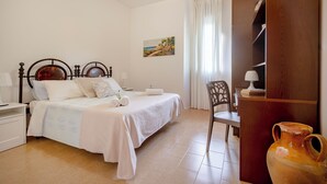 Een slaapkamer met een bed, een stoel, een nachtkastje, een lamp, een schilderij en een houten kast.