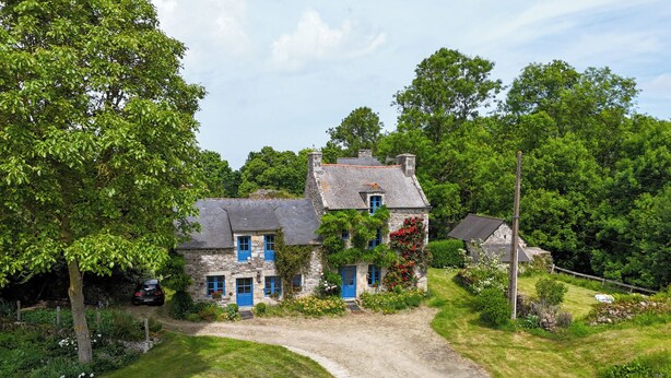 A stone house with blue shutters, surrounded by lush greenery and a gravel driveway. - Gîte du Château de Montafilan (Corseul)