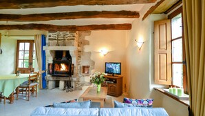 A cozy living room with a stone fireplace, wooden beams, a television, and comfortable seating. - Gîte du Château de Montafilan (Corseul)