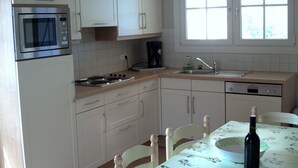 A kitchen with white cabinets, a microwave, a stove, a sink, and a dining table with chairs. - Le Sapin B : Mooie Vakantiewoning met Zwembad in de Ardèche (Chassagnes)
