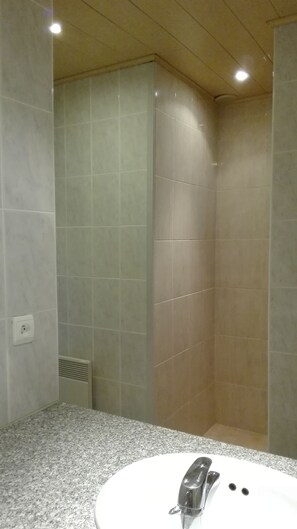 Une salle de bain dotée d’un comptoir en granit, d’un lavabo blanc et d’un espace douche aux carreaux beiges.