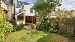 A modern house with a spacious patio, a small garden, and a large window overlooking the yard. - Central Wimbledon House Sleeps 8 - Secluded Garden (London)