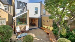 A modern house with a patio, seating area, and a view of the garden. - Central Wimbledon House Sleeps 8 - Secluded Garden (London)