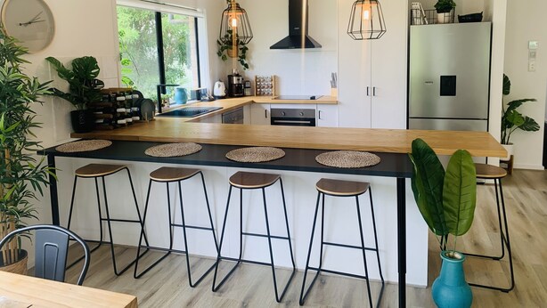 A modern kitchen with a central island, bar stools, hanging pendant lights, and a large window. - Modern country house set in the heart of the vines (McLaren Flat)