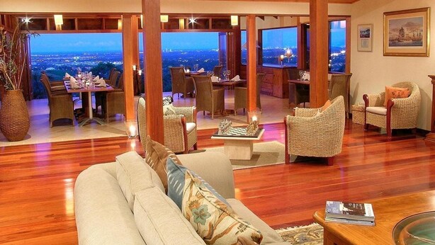 Amplia sala de estar con techo de madera, muebles de mimbre y un ventanal con vista a la ciudad.