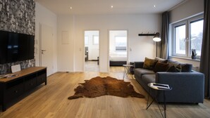 Ett modernt vardagsrum med en stor TV med platt skärm, en grå soffa, en brun lädermatta och en möbel i trä för förvaring av underhållningsutrustning.