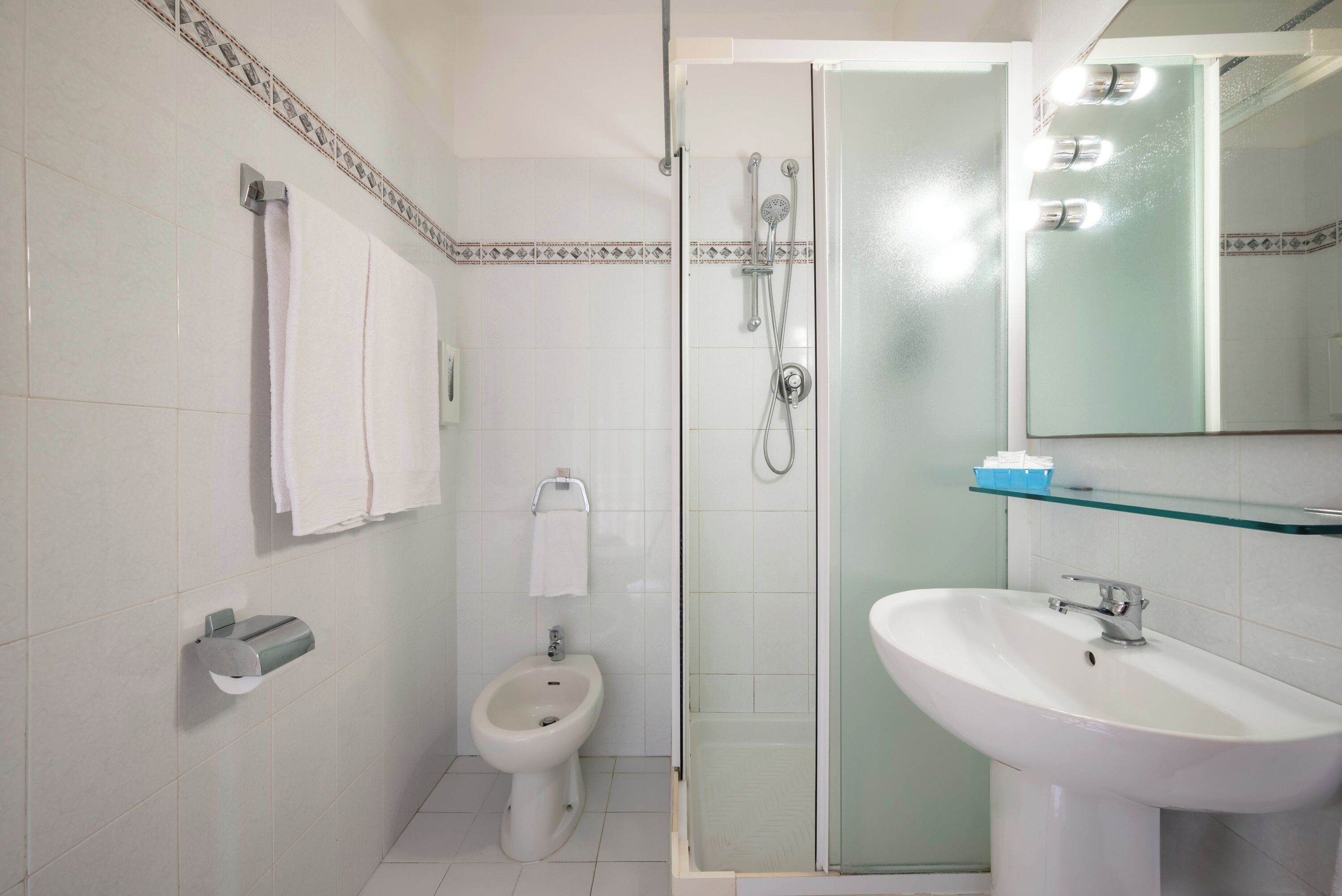 Un baño con bidé, cabina de ducha de vidrio, lavamanos y espejo con luces.