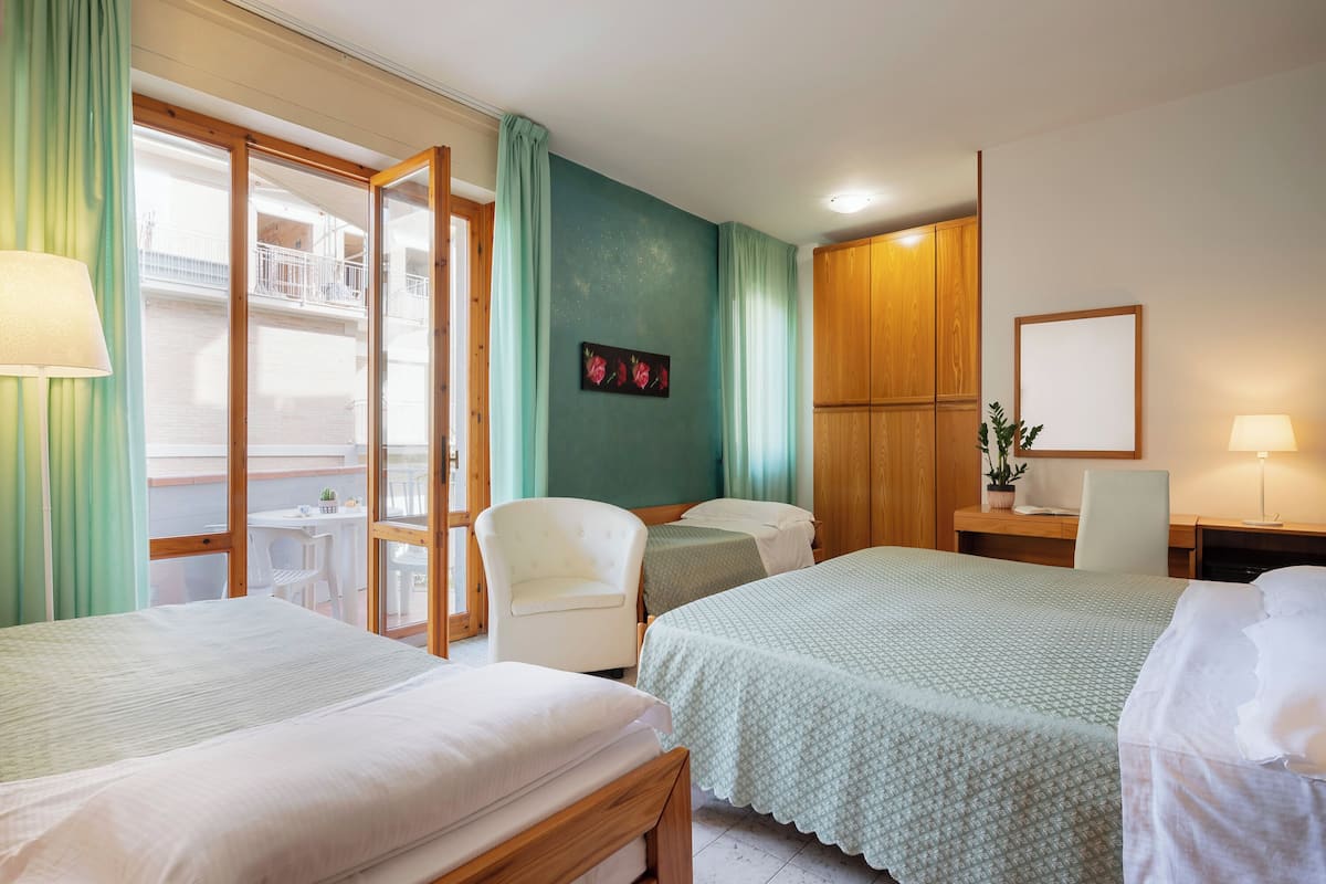 A hotel room with two beds, a desk, a chair, and a balcony with a table and chairs.
