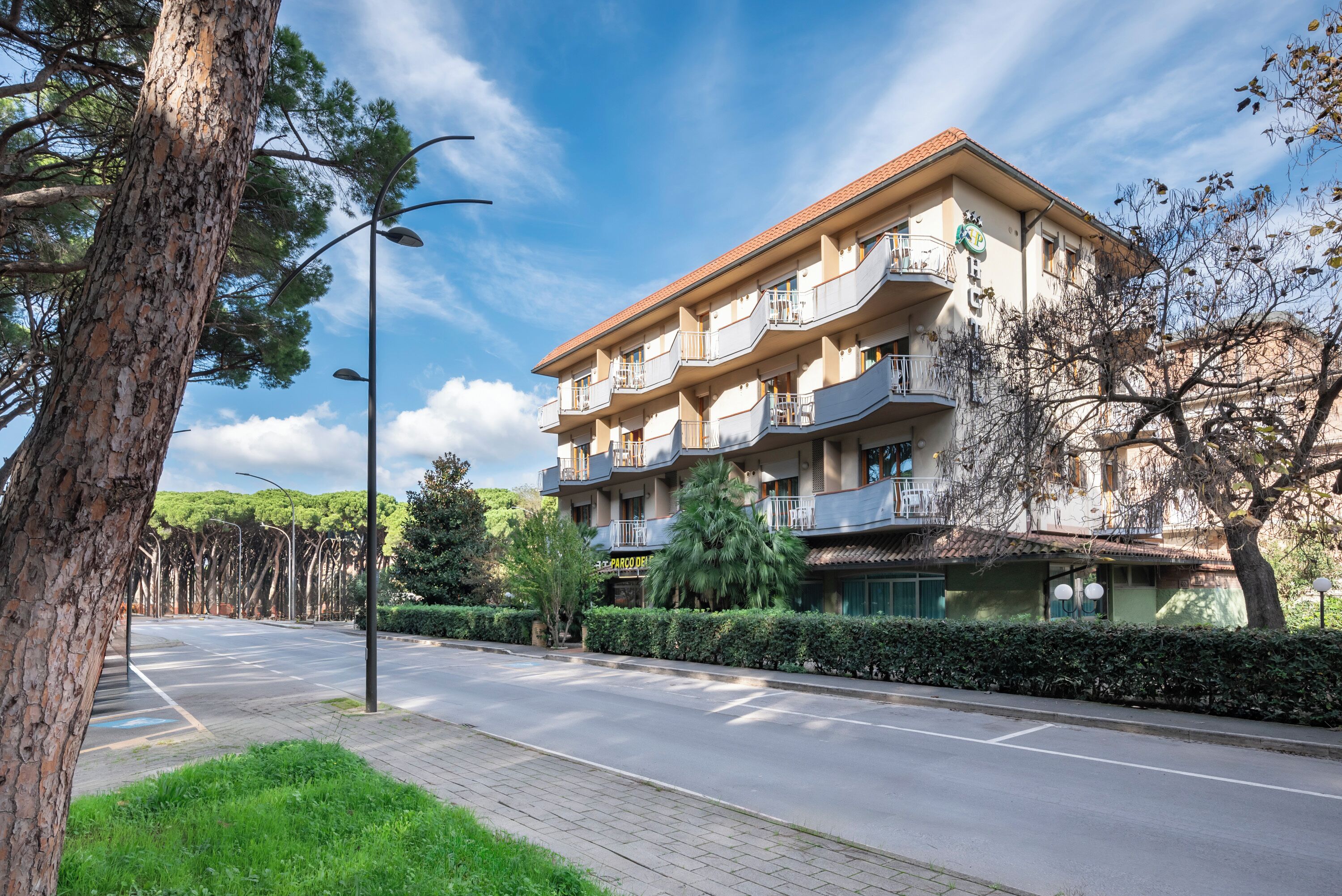 Un hôtel à plusieurs étages doté de balcons, avec un ciel dégagé et un jardin bien entretenu.