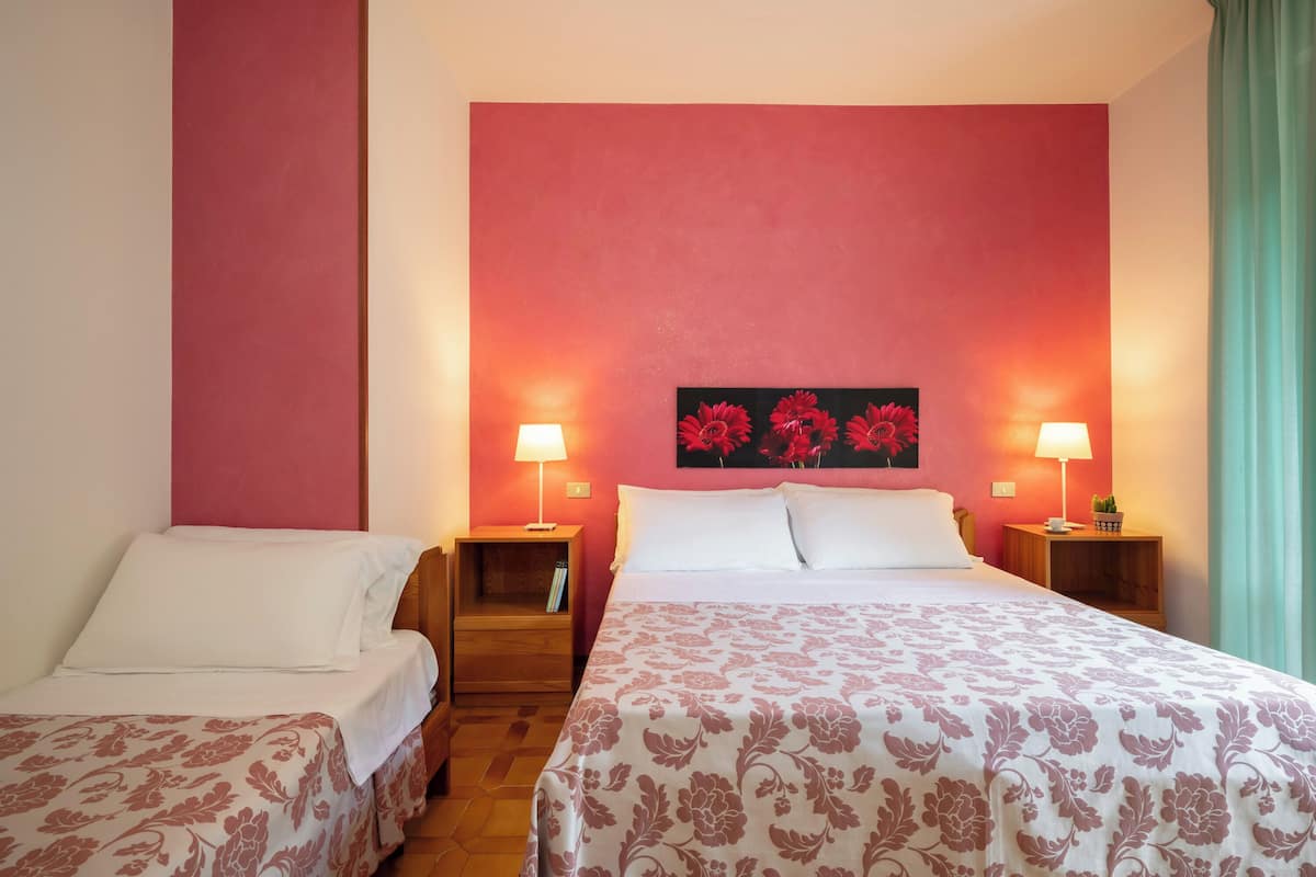 A hotel room with two beds, a red accent wall, and a floral painting above the beds.