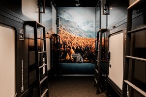 A train carriage interior with luggage storage compartments and a scenic mural of a forest and mountains. - Capsule Hotel - Zurich Airport (Kloten)