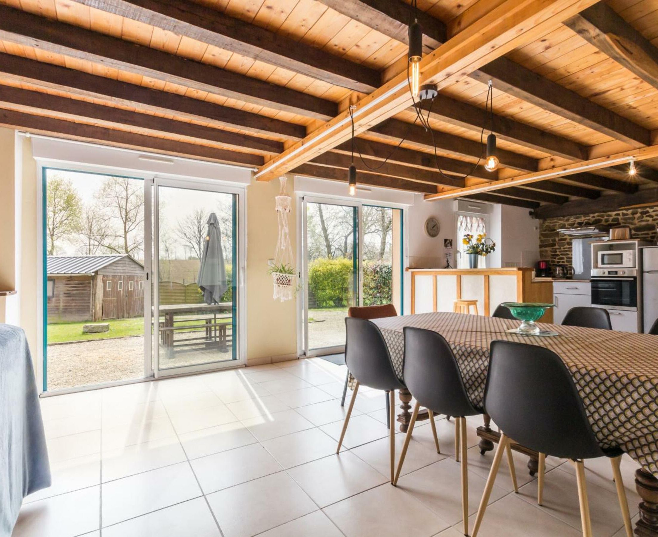 Een ruime keuken met moderne apparatuur, een eetgedeelte met een grote tafel en stoelen, en uitzicht op de omgeving via grote schuifdeuren.