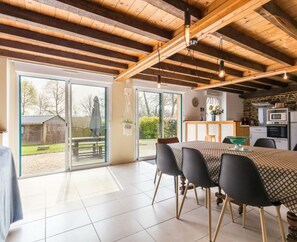 Une cuisine spacieuse équipée d’appareils électroménagers modernes, un coin repas avec une grande table et des chaises, et une vue sur l’extérieur grâce à de grandes portes-fenêtres coulissantes.
