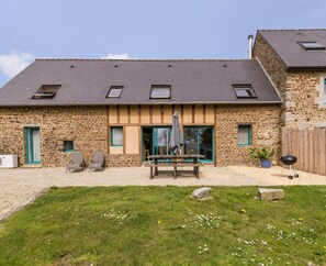 Un bâtiment en pierre avec un toit en pente, une terrasse avec une table et des chaises, et un barbecue.
