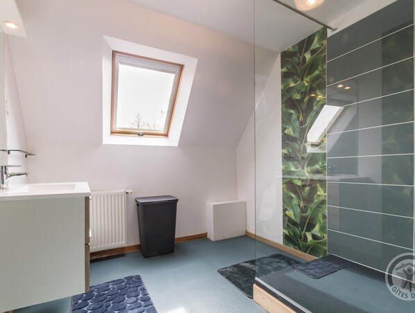 A modern bathroom with a skylight, a radiator, a trash bin, and a glass shower enclosure with a green leaf pattern.