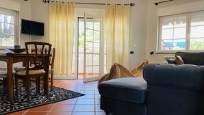 A living room with a sofa, a dining table with chairs, a TV, and a sliding glass door leading to an outdoor area. - The Quiet Loft Golf & Beach resort (Amoreira)