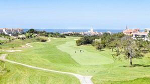 A golf course with a clear path, a few players, and buildings in the background. - The Quiet Loft Golf & Beach resort (Amoreira)