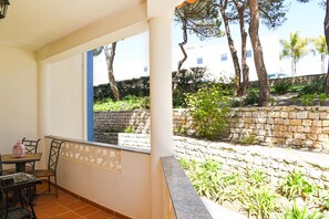 Un balcon avec une table et des chaises, donnant sur un jardin agrémenté de murs en pierre et d’arbres.