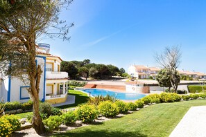 Un espace piscine avec un ciel d’un bleu limpide, une pelouse bien entretenue et un bâtiment à la façade jaune et bleue.