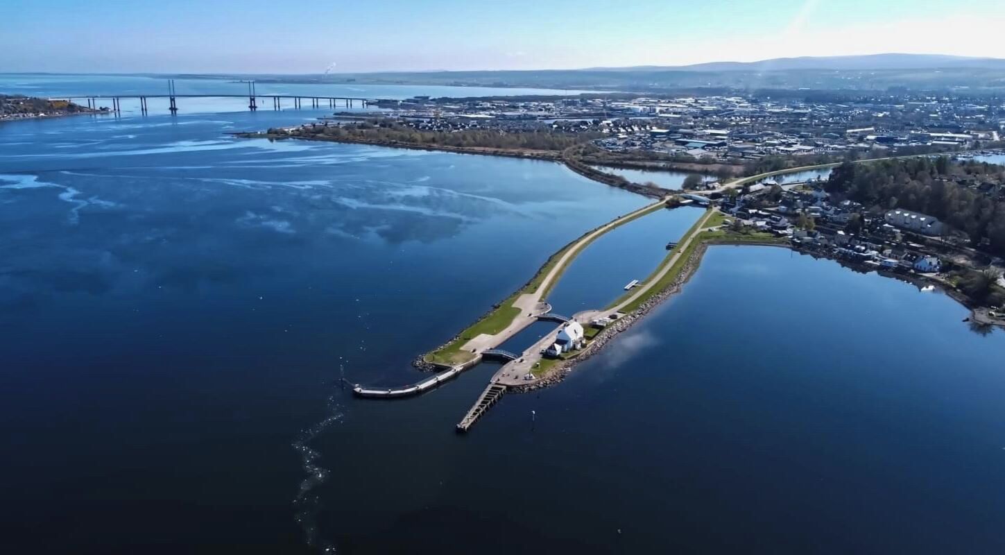 An aerial view of a coastal area with a bridge, a marina, and a residential area.