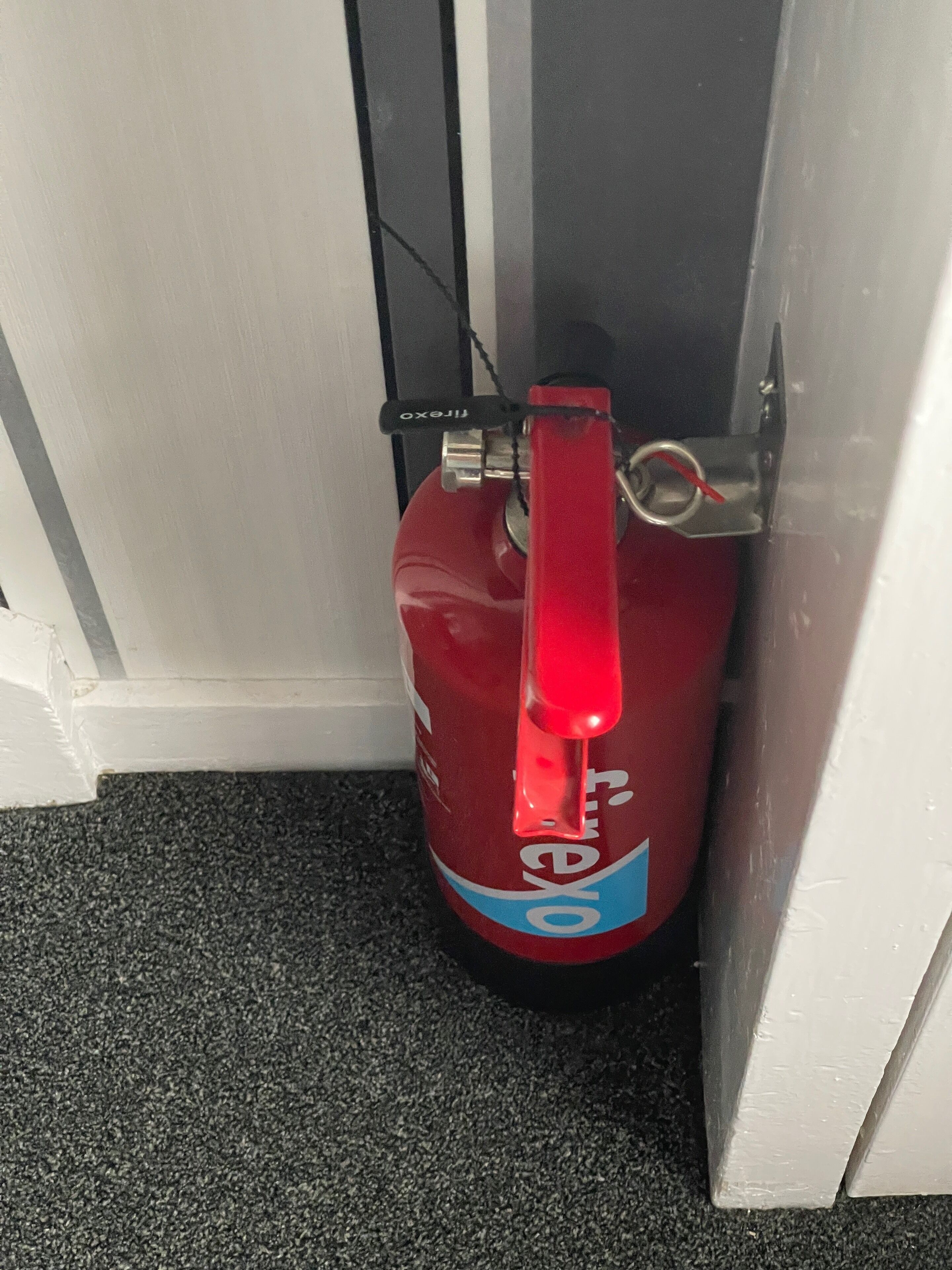 Un extincteur rouge est placé devant une porte blanche.