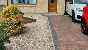 A two-story house with a gravel driveway and a paved path leading to the door. - 2 Bedroom House  with the Caledonian Canal at rear. (Inverness)
