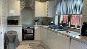 A modern kitchen with white cabinets, a microwave, a stove, and a sink. - 2 Bedroom House  with the Caledonian Canal at rear. (Inverness)