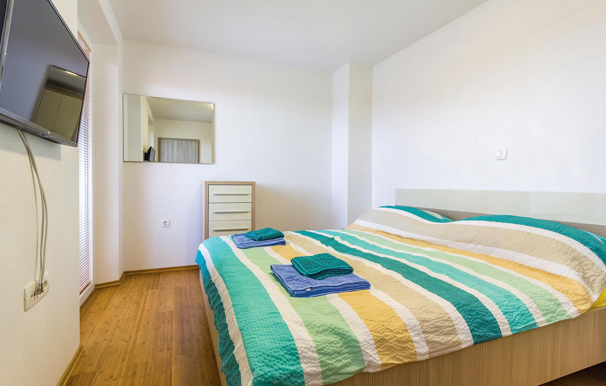 Een slaapkamer met een bed, nachtkastje, spiegel en een aan de muur bevestigde televisie.