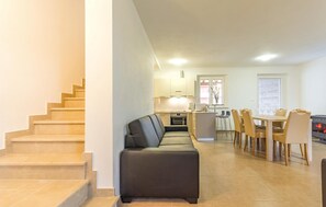 Een modern appartement met een trap, een bank, een eethoek met stoelen en een tafel, en een keuken met kasten en apparatuur.