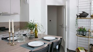 A modern kitchen with a dining table set for two, featuring a white plate, two candles, a wine bottle, and a vase with green plants. - Apt. Neuf à 50m du Port - Parking Privé, Ascenseur (Saint-Valery-sur-Somme)