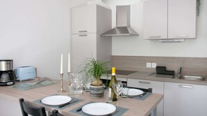 A modern kitchen with white cabinets, a stainless steel range hood, and a dining area set with plates, cutlery, and a bottle of wine. - Apt. Neuf à 50m du Port - Parking Privé, Ascenseur (Saint-Valery-sur-Somme)